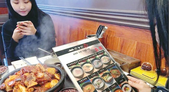 Many Koreatown businesses are making an effort to understand the consuming habits of their Chinese customers. The photo is showing customers looking through a Chinese-language menu at a Korean restaurant.