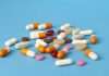US Prescription Drug Prices Under Fire: $15K Meds Sold for $40 US drug price hikes symbolized by assorted pills scattered on a blue background