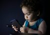 LAUSD Screen Time Policy Divides Parents Over Device Limits boy in blue tank top holding black iphone 5