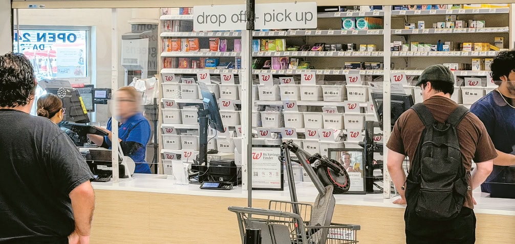 Customers waiting at a pharmacy prescription pickup counter amid rising health insurance denials for brand-name drugs.